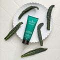 Sukin Super Greens Detoxifying Facial Scrub with kale leaves on a white background