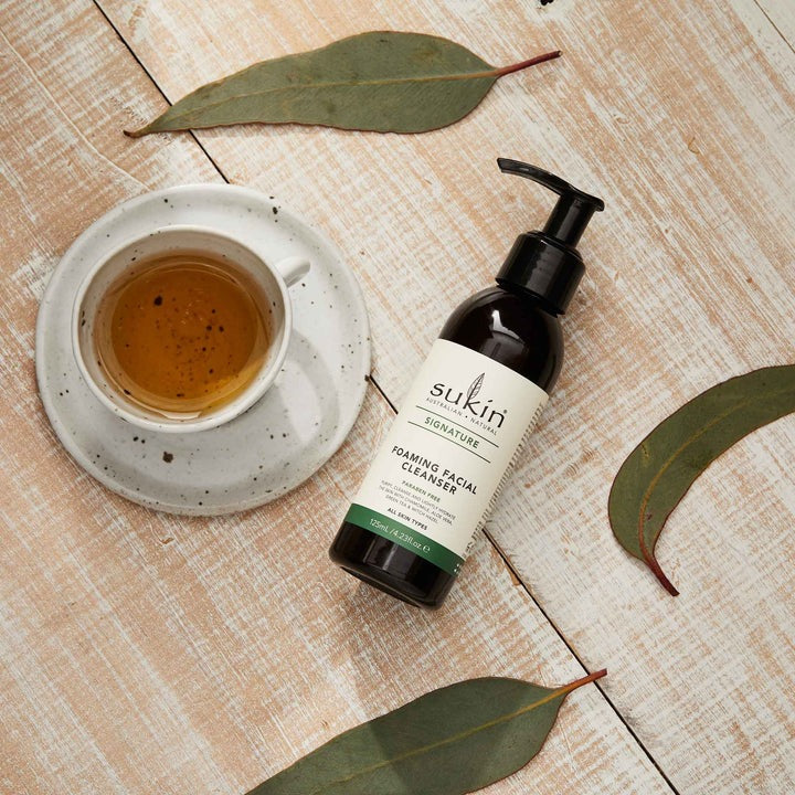 Sukin skincare bottle with a cup of tea and leaves on a wooden surface