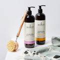 Two bottles of Sukin body lotion with a brush and towel on a light background