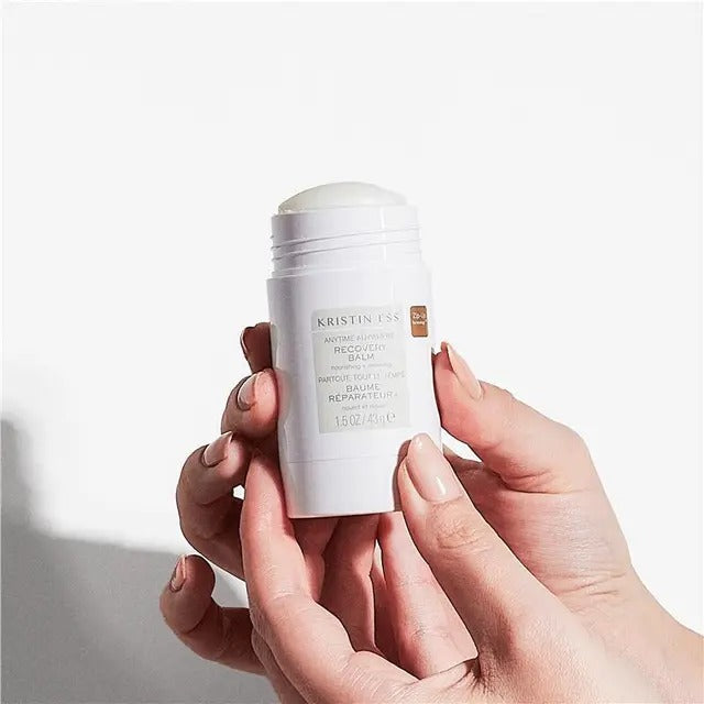 Hand holding a white skincare balm stick with visible branding on a light background