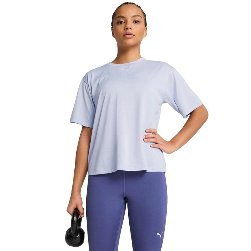 Woman wearing a light blue athletic shirt and purple leggings holding a black kettlebell on a white background