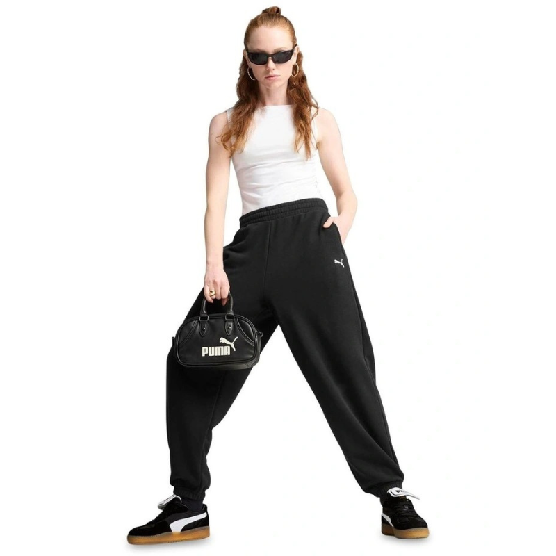 Person wearing black Puma pants and a white tank top, holding a black Puma handbag on a white background.
