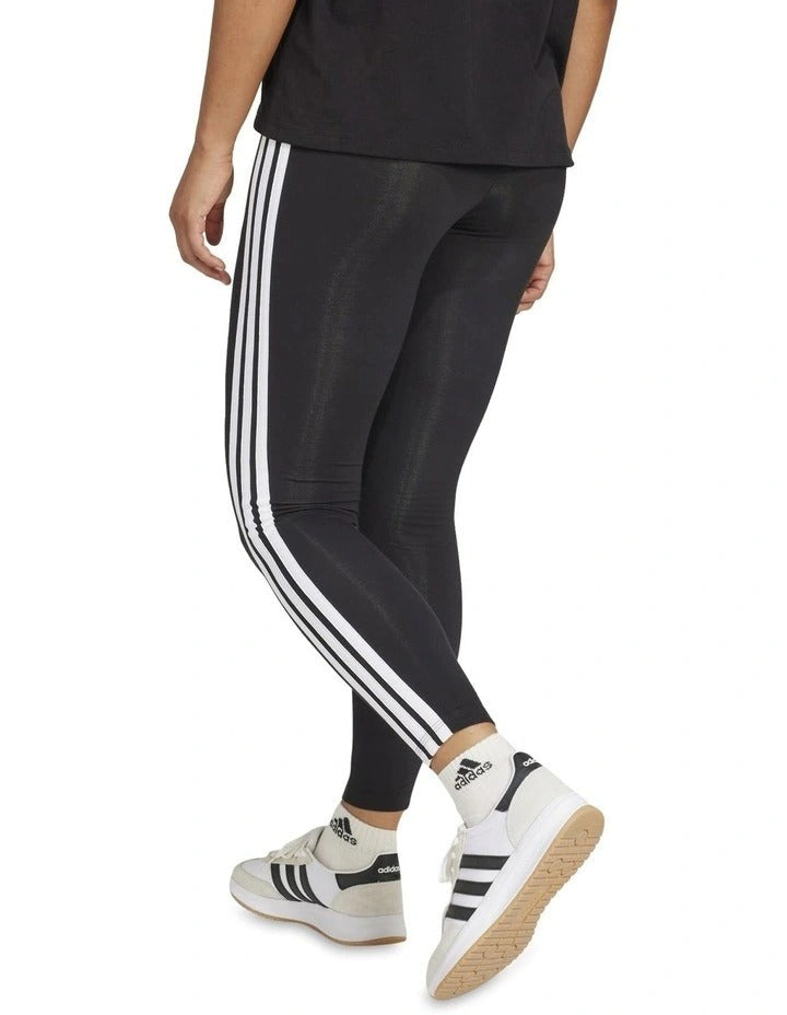 Person wearing black Adidas leggings with white stripes on a white background