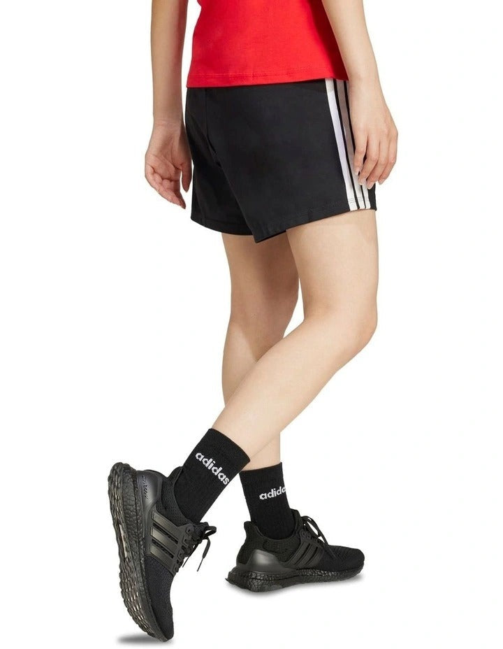 Person wearing black Adidas shorts and shoes on a white background