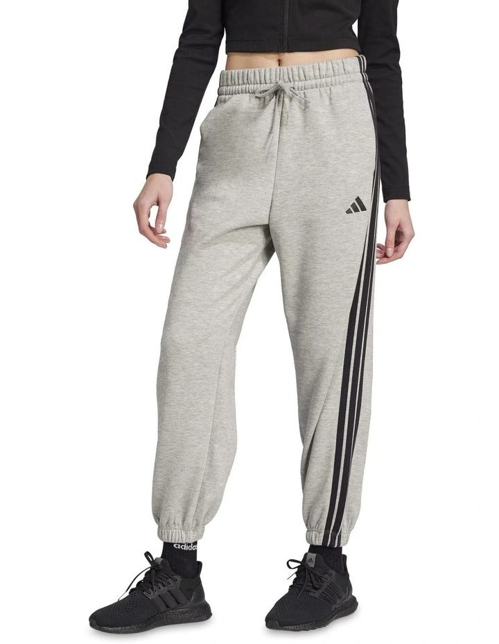 Person wearing black Adidas tracksuit pants with white stripes and white sneakers on a white background